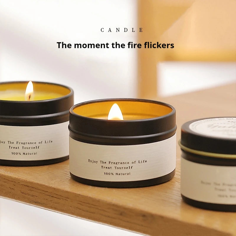 Three candles in tin containers with visible flames on a wooden surface, featuring text about the fragrance of life.