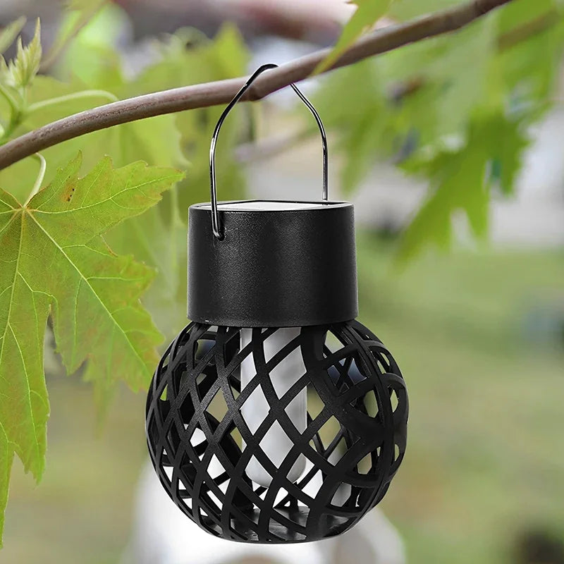 Black lattice-patterned solar lantern hanging from a branch with green leaves.