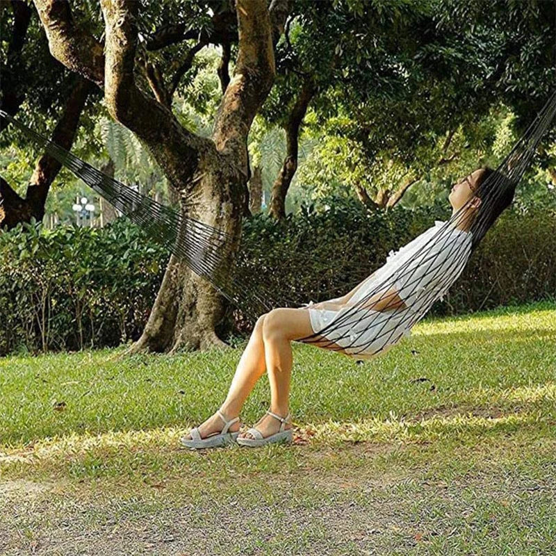 Person relaxing in a hammock under a tree in a park