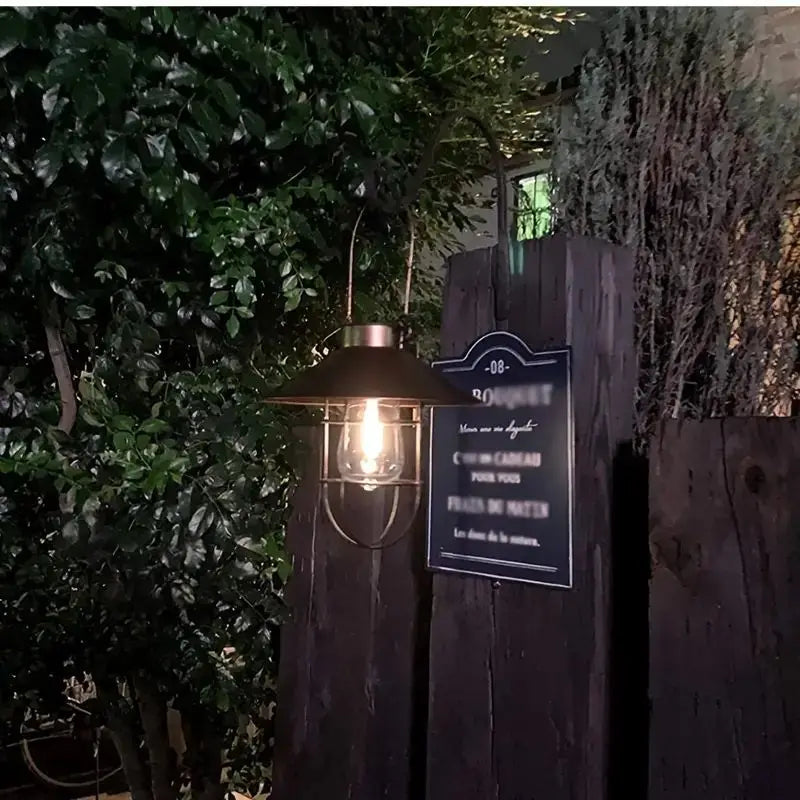 Decorative outdoor light fixture with a sign on a wooden post at night.
