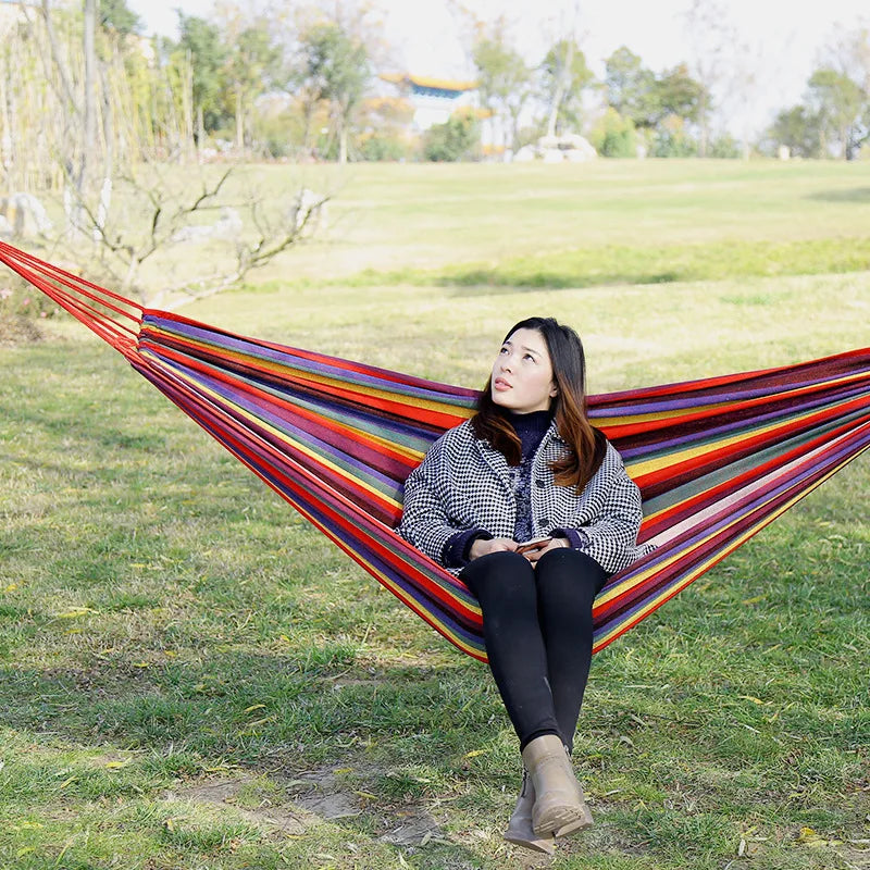Woman sitting in a colorful hammock in a grassy field