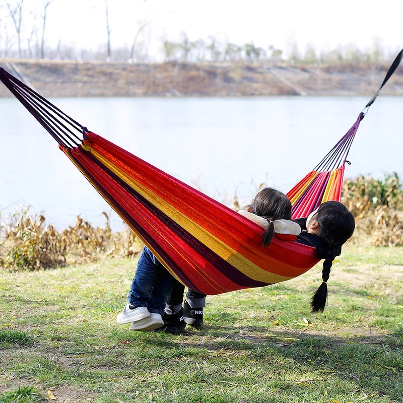 Two children in a red and yellow striped hammock by a lake.