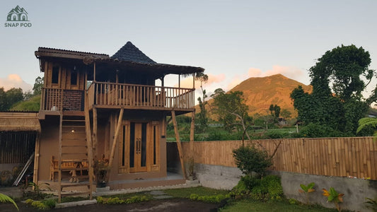 A two-storey wooden and bamboo house in Bali with a mountain glowing in sunset light.