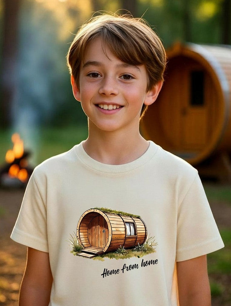 Happy 13-year-old boy wearing a cream "Home from home" barrel pod t-shirt, standing in a beautiful woodland glamping scene with a wooden barrel pod and campfire in the background.