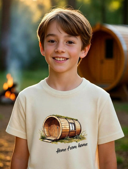 Happy 13-year-old boy wearing a cream "Home from home" barrel pod t-shirt, standing in a beautiful woodland glamping scene with a wooden barrel pod and campfire in the background.