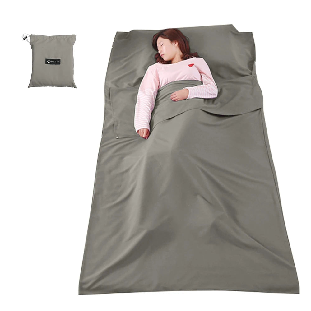 Person lying on a gray sleeping bag with a matching pillow on a white background