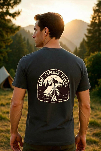 Rear view of a man wearing a dark charcoal grey CAMP. EXPLORE. REPEAT. vintage camping t-shirt in a scenic mountain camping setting at golden hour