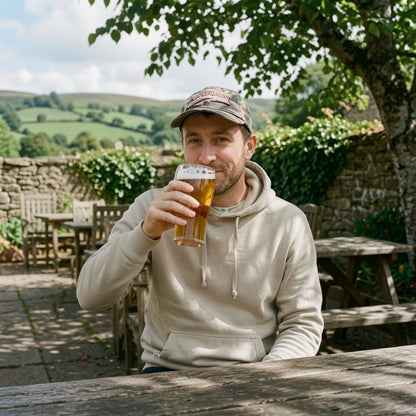 Man holding a beer mug outdoors with greenery and stone wall in the background