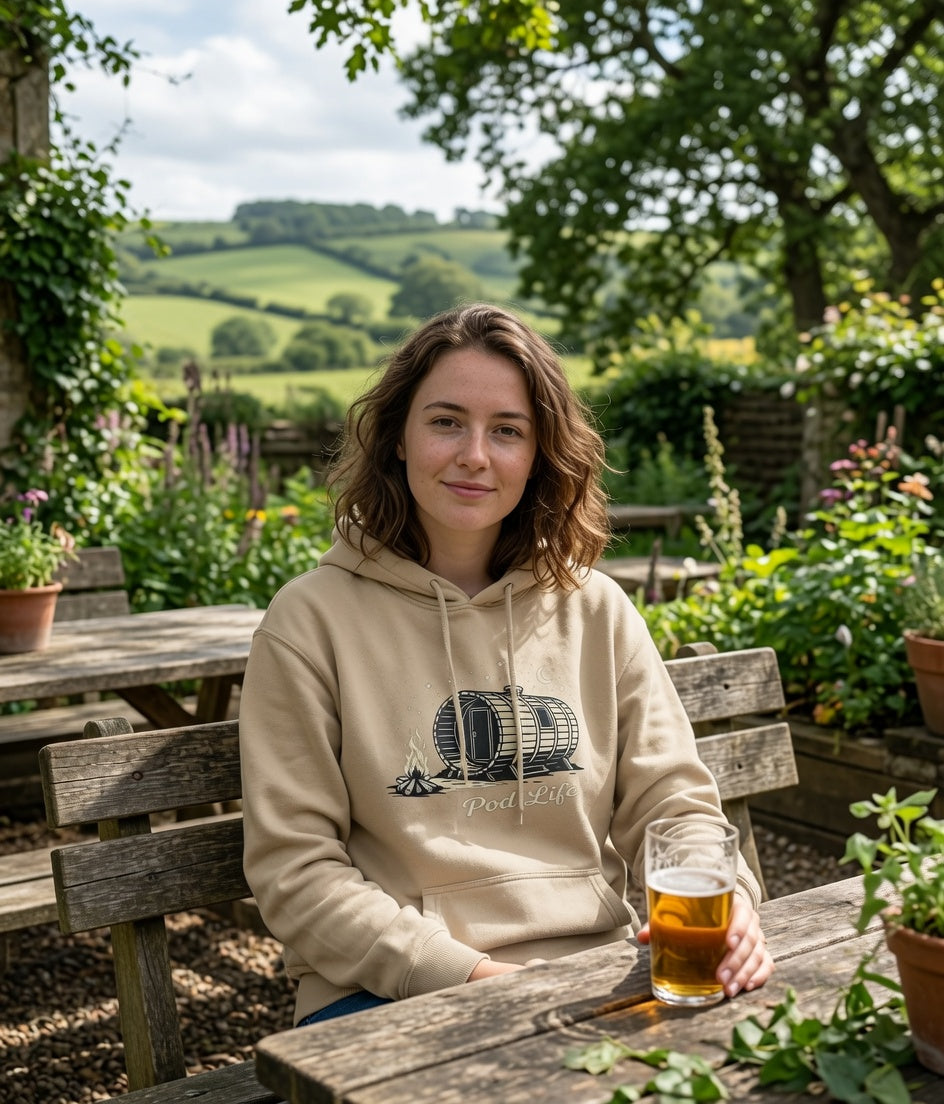 Woman in a beige hoodie with a caravan design, sitting outdoors with a drink.