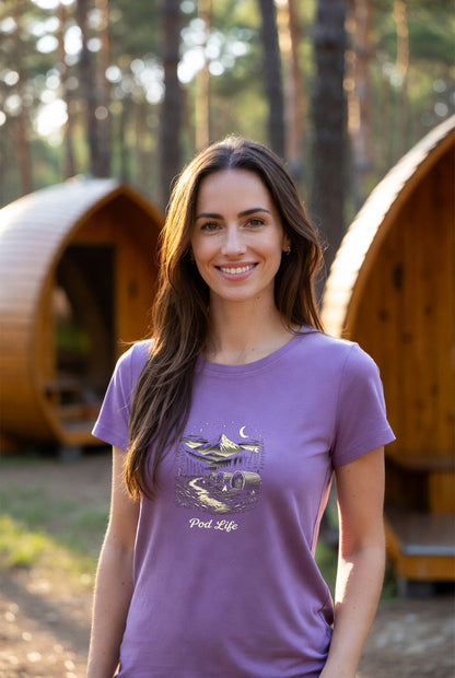 Beautiful woman wearing a plain lavender organic t-shirt in a beautiful woodland glamping setting with barrel pods in the background at golden hour.